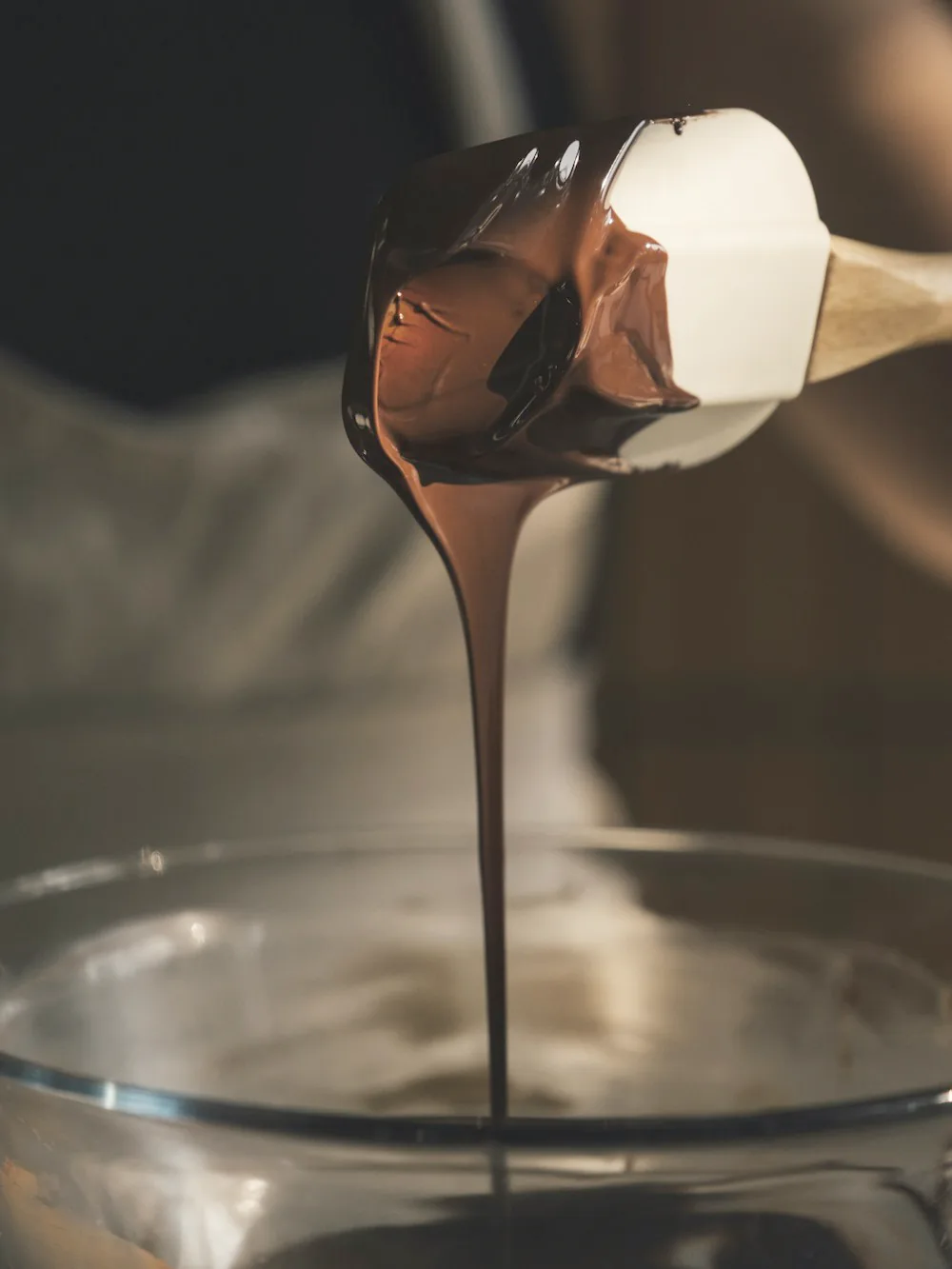 Chocolate fundido cayendo en hilo desde una jarra a un bol de cristal.