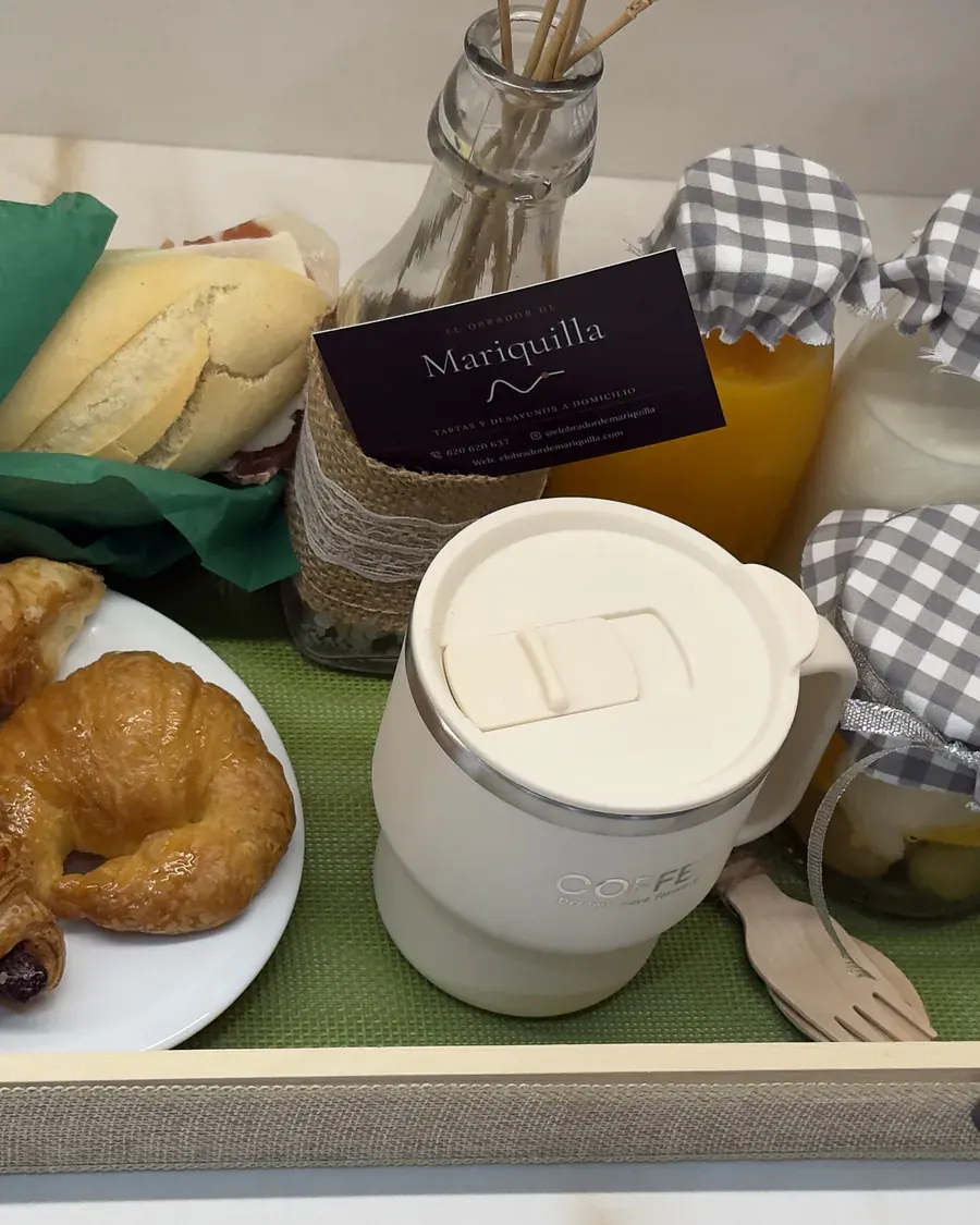 Detalle de la bandeja dulce: taza de café, croissant, zumo de naranja y la tarjeta de El Obrador de Mariquilla.