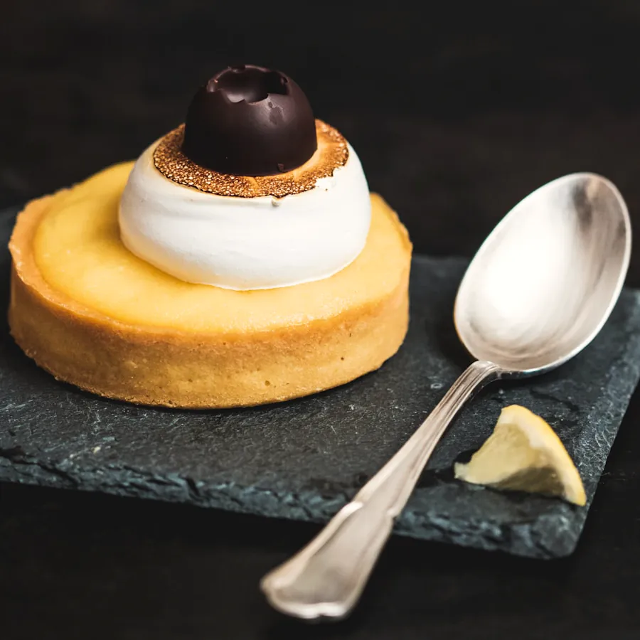 Pastel individual con merengue tostado y una bola de chocolate, sobre pizarra.