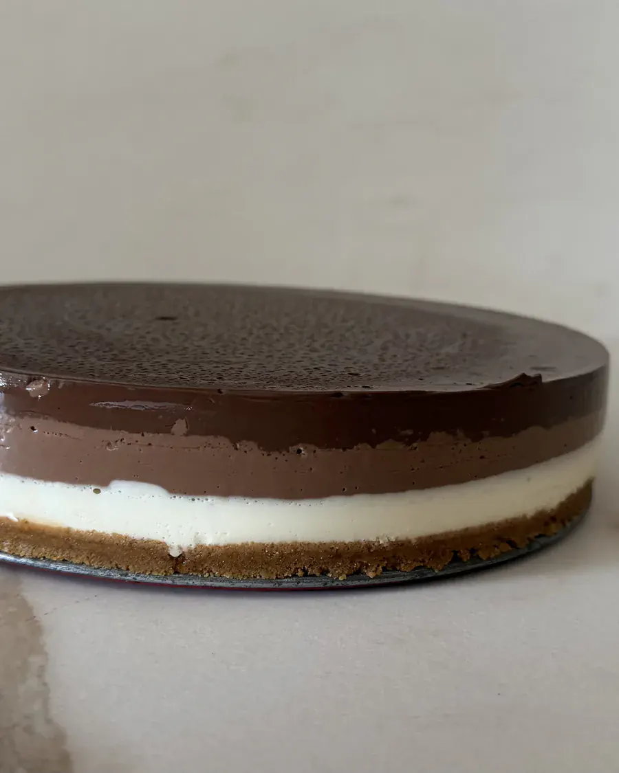Tarta de tres chocolates entera vista de perfil, con la capa de chocolate negro brillante encima de la blanca y la con leche.