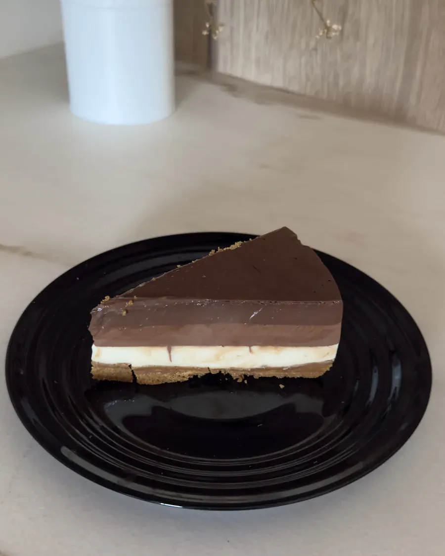 Porción de tarta de tres chocolates vista desde arriba en un plato negro sobre la encimera de mármol.