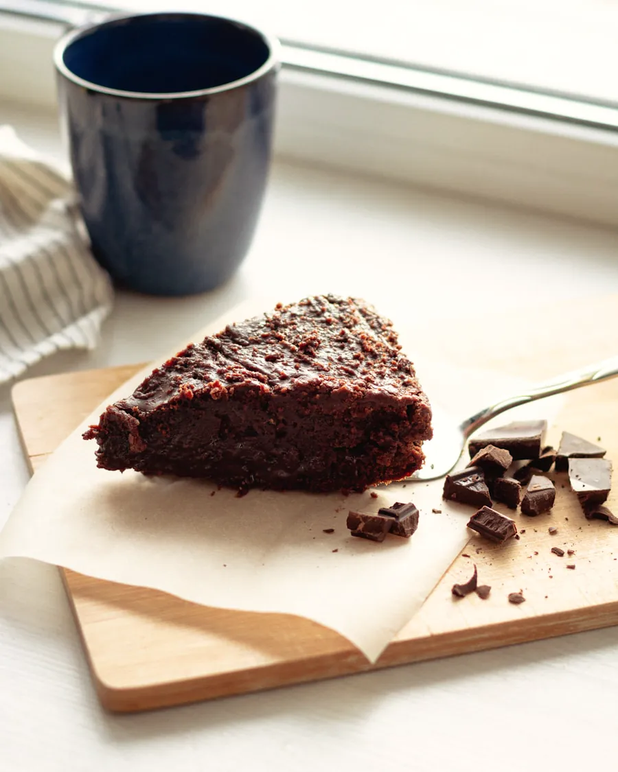 Porción de tarta de chocolate sobre papel de horno, con trozos de chocolate al lado.