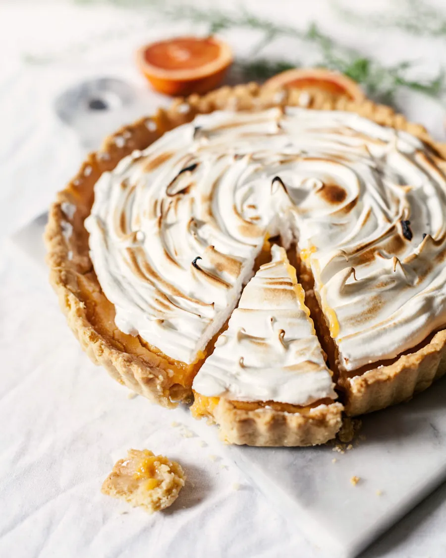 Tarta de limón con merengue tostado en espiral, con una porción cortada, sobre un paño claro.