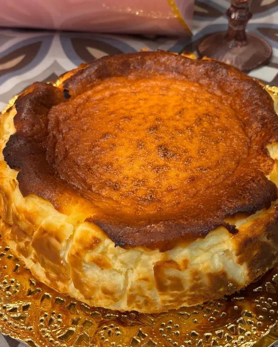 Tarta de queso al estilo La Viña entera, alta y con la superficie tostada, sobre bandeja dorada.