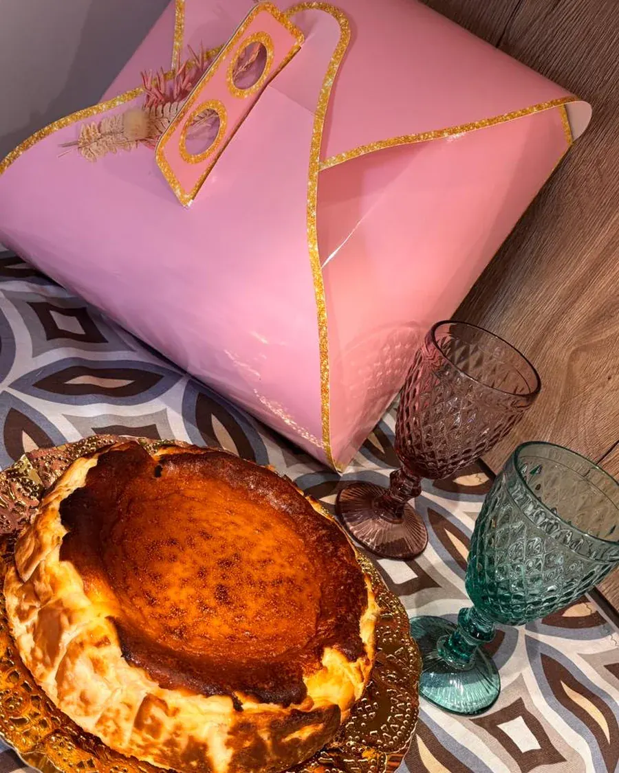 Tarta de queso con una porción cortada, junto a su caja de reparto en papel rosa.
