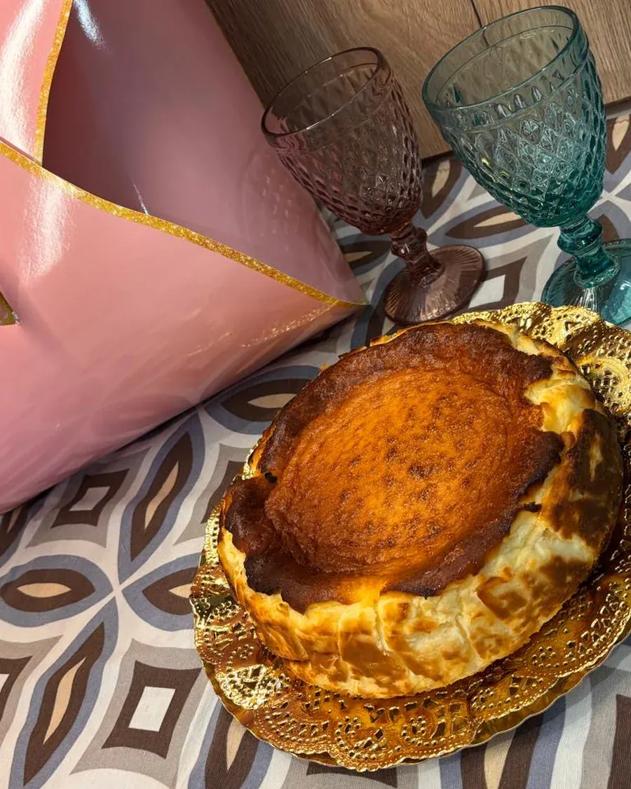 Tarta de queso servida en bandeja dorada, con el envoltorio de reparto y copas de cristal detrás.