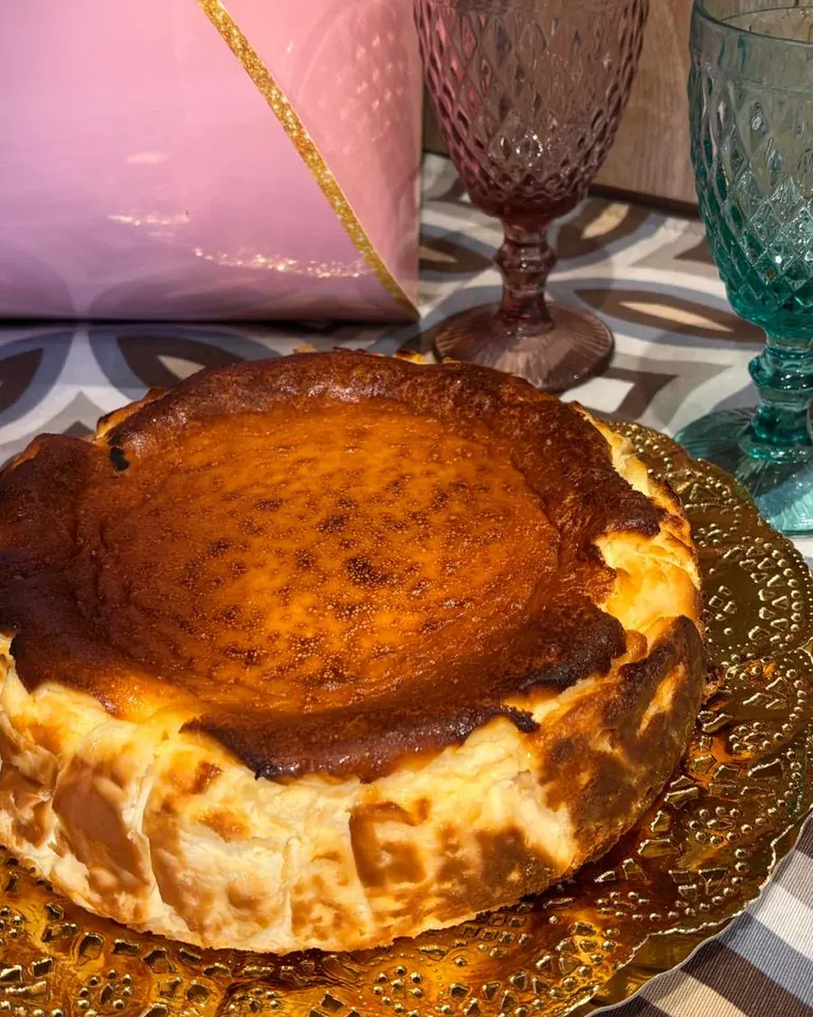 Tarta de queso entera lista para entregar, con el envoltorio rosa y copas verdes al fondo.