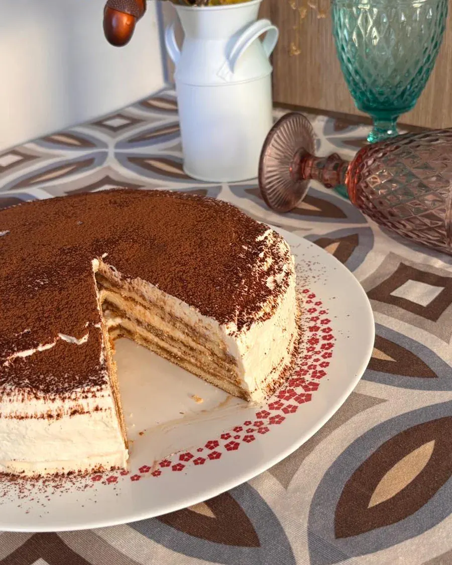 Tiramisú entero con una porción cortada, en plato blanco, con las capas de bizcocho a la vista.