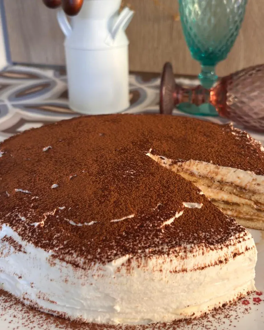 Tiramisú cubierto de cacao espolvoreado, servido en plato blanco.
