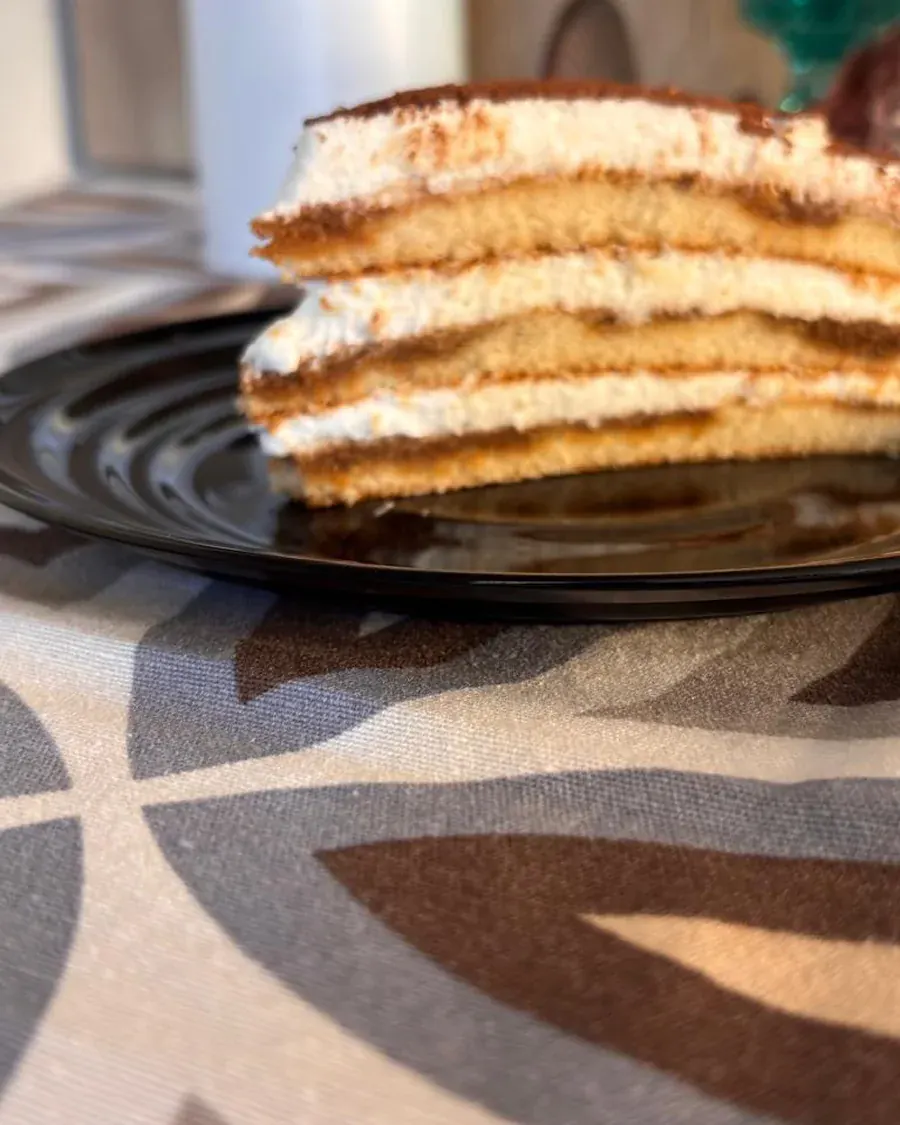 Porción de tiramisú en plato oscuro, con las capas de bizcocho y crema bien marcadas.