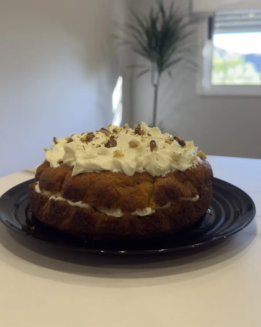 Carrot cake entera, con crema de queso y nueces troceadas por encima, sobre un plato negro.