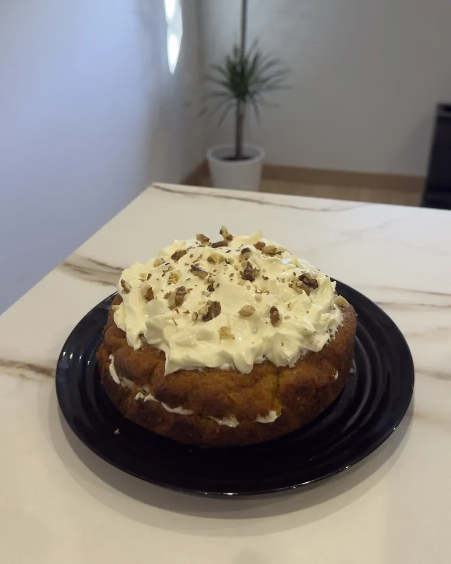 Carrot cake entera vista desde arriba, cubierta de crema de queso y nueces, sobre encimera de mármol.